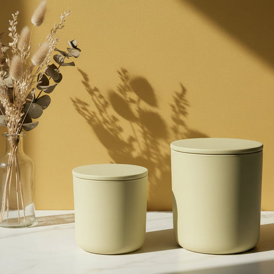 Two beige containers with lids on a white surface against a green wall.